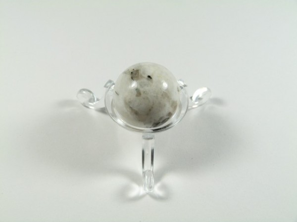 Kula kamień księżycowy rainbow moonstone o średnicy 2,5 cm. Biała kula z kamienia na przezroczystym stojaku, ustawiona na białym tle.