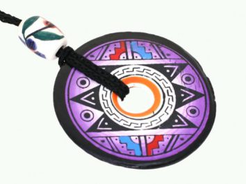 Okrągły, kolorowy wisiorek z geometrycznym wzorem, zawieszony na czarnym sznurku.