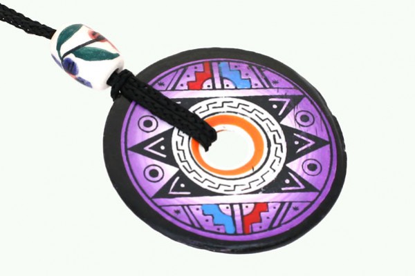 Okrągły, kolorowy wisiorek z geometrycznym wzorem, zawieszony na czarnym sznurku.