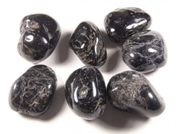 Siedem wypolerowanych, czarnych kamieni leży na białym tle.