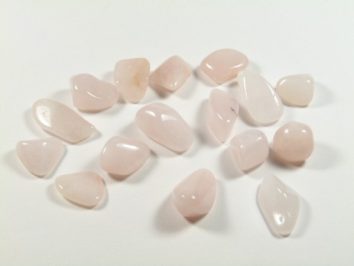 Petalit - kamień gładzony, polerowany, szlifowany. Różowe, gładkie kamienie leżą rozrzucone na białym tle.