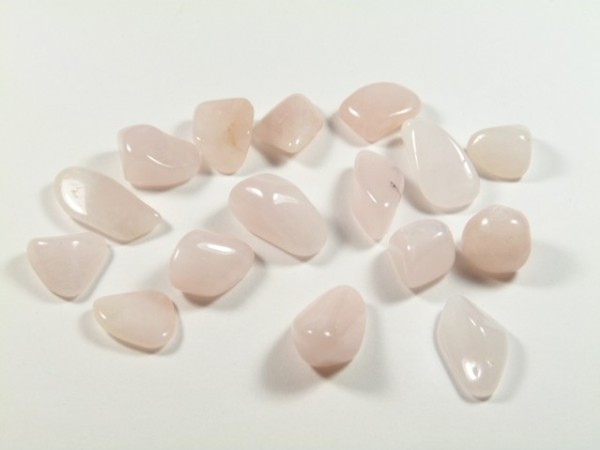 Petalit - kamień gładzony, polerowany, szlifowany. Różowe, gładkie kamienie leżą rozrzucone na białym tle.