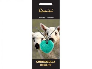 Dwie owce w tle, na pierwszym planie zielony wisiorek w kształcie serca na sznurku.