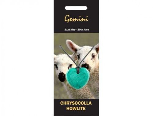 Dwie owce w tle, na pierwszym planie zielony wisiorek w kształcie serca na sznurku.