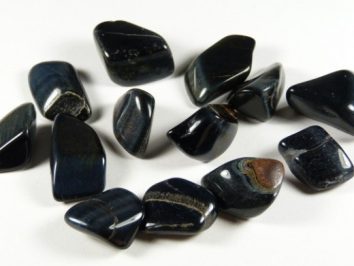 Wypolerowane kamienie niebieskiego tygrysiego oka leżące na białym tle.