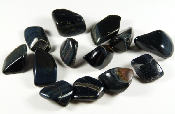 Wypolerowane kamienie niebieskiego tygrysiego oka leżące na białym tle.
