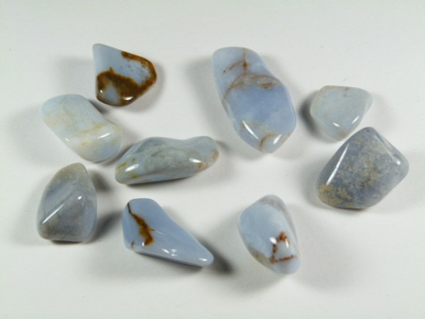 Osiem niebieskich, wypolerowanych kamieni leży na białym tle.