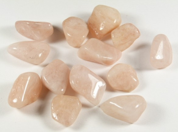 Jasnoróżowe, oszlifowane kamienie leżące na białym tle.