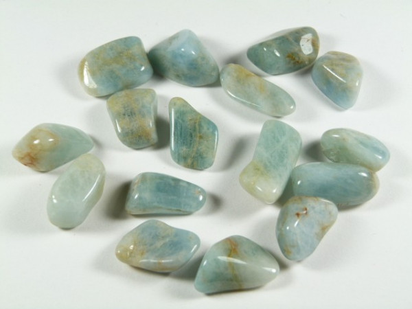 Kilka wypolerowanych, jasnozielonych kamieni leży rozproszonych na jasnym tle.