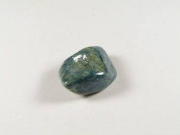 Wypolerowany, niebiesko-zielony kamień leży na białym tle.
