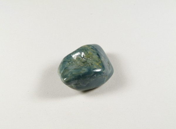 Wypolerowany, niebiesko-zielony kamień leży na białym tle.