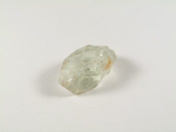 Przezroczysty, surowy kryształ leży na białym tle.