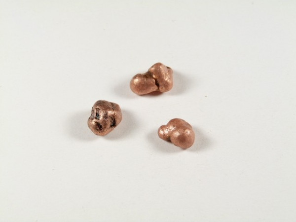 Miedź - kamień naturalny, surowy, nieszlifowany. Trzy małe, nieregularne bryłki miedzi leżą na białym tle.