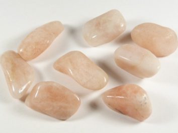 Osiem wypolerowanych, jasnoróżowych kamieni leży na białym tle.