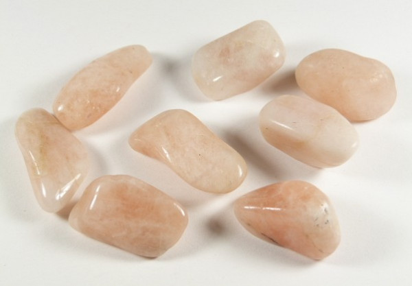 Osiem wypolerowanych, jasnoróżowych kamieni leży na białym tle.