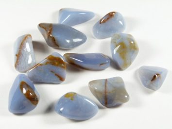 Kilka niebieskich, oszlifowanych kamieni z brązowymi żyłkami na białym tle.