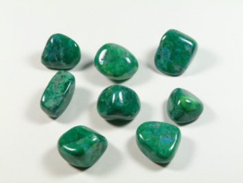Howlit chryzokola - kamień gładzony, polerowany, szlifowany i bębnowany w formie otoczaka. Osiem zielonych, wypolerowanych kamieni leży na białym tle.