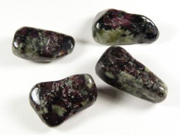 Cztery wypolerowane kamienie zoisytu z rubinem na białym tle.
