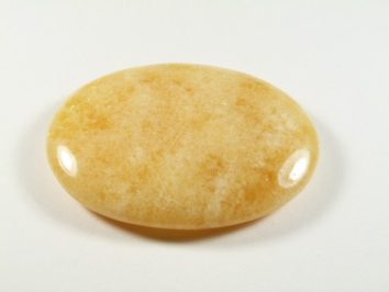 Kalcyt złoty - kamień gładzony, polerowany, szlifowany. Gładki, żółty, owalny kamień leży na białym tle.
