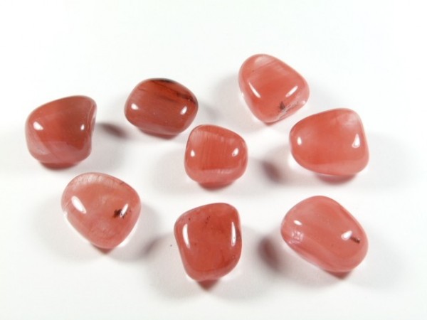 Kwarc wiśniowy - kamień gładzony, polerowany, szlifowany i bębnowany w formie otoczaka. Osiem różowych, wypolerowanych kamieni leży na białym tle.