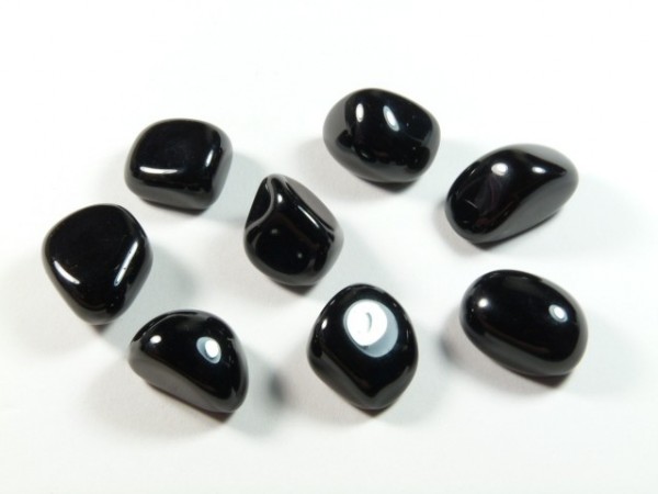 Onyks czarny - kamień gładzony, polerowany, szlifowany i bębnowany w formie otoczaka. Osiem polerowanych, czarnych kamieni leży na białym tle.