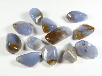 Polerowane kamienie chalcedonu o niebiesko-brązowym zabarwieniu, ułożone na białym tle.