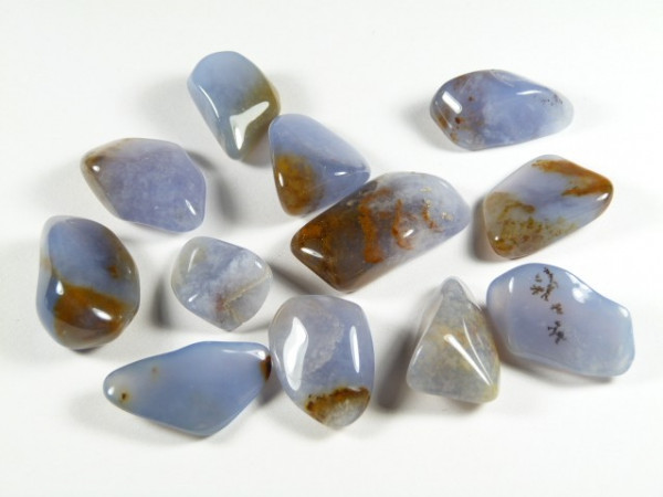 Polerowane kamienie chalcedonu o niebiesko-brązowym zabarwieniu, ułożone na białym tle.