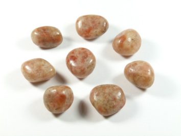 Kamień słoneczny - kamień gładzony, polerowany, szlifowany i bębnowany w formie otoczaka. Osiem polerowanych kamieni słonecznych ułożonych na białym tle.