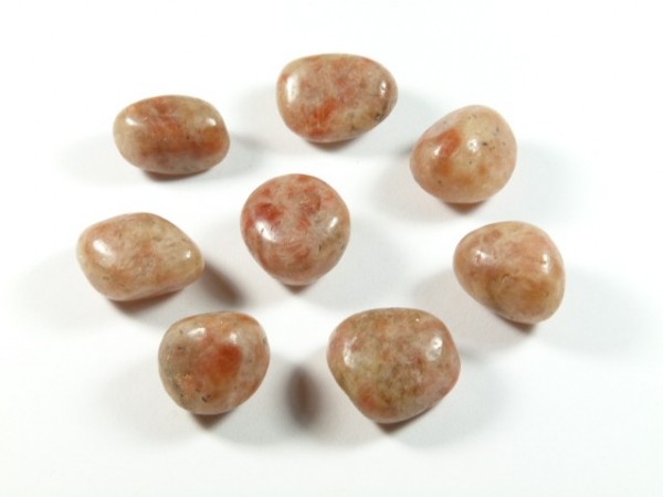 Kamień słoneczny - kamień gładzony, polerowany, szlifowany i bębnowany w formie otoczaka. Osiem polerowanych kamieni słonecznych ułożonych na białym tle.