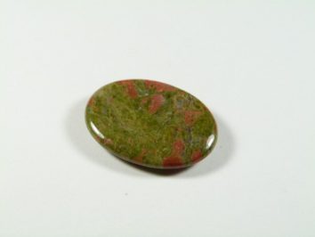 Unakit - płaski, szlifowany kamień. Owalny, polerowany kamień o zielono-czerwonym zabarwieniu na białym tle.