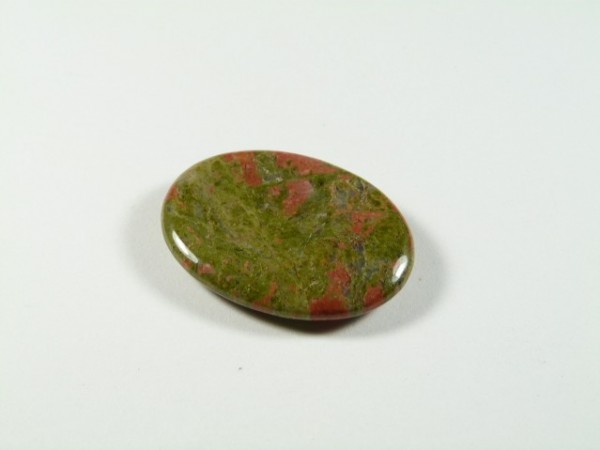 Unakit - płaski, szlifowany kamień. Owalny, polerowany kamień o zielono-czerwonym zabarwieniu na białym tle.