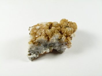 Syderyt - kamień naturalny, surowy, nieszlifowany. Kawałek minerału o żółtobrązowych kryształach na białym tle.