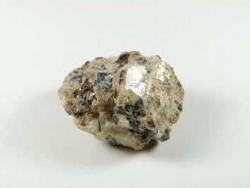 Safirin - kamień naturalny, surowy, nieszlifowany. Nieregularny kamień z jasnymi i ciemnymi plamami na białym tle.