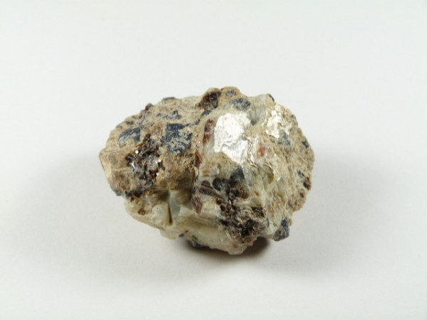 Safirin - kamień naturalny, surowy, nieszlifowany. Nieregularny kamień z jasnymi i ciemnymi plamami na białym tle.