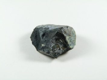 Callaghanit kamień. Czarny, nieregularny kamień leży na białym tle.