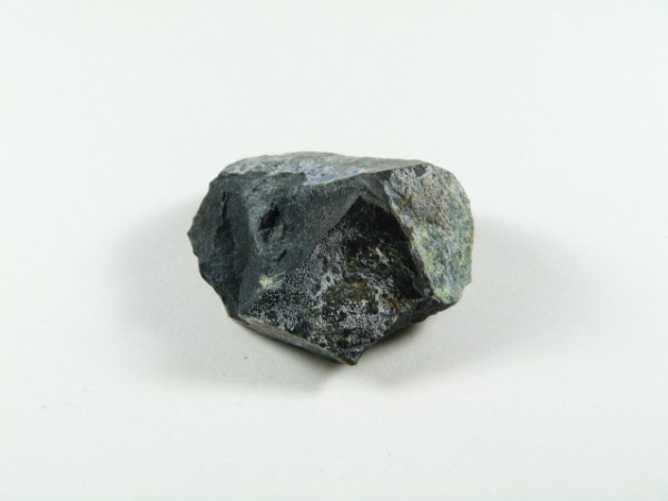 Callaghanit kamień. Czarny, nieregularny kamień leży na białym tle.