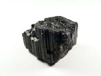 Czarny turmalin - kamień naturalny, surowy, nieszlifowany. Czarny kryształ turmalinu na białym tle.