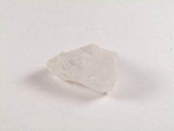 Przezroczysty, nieregularny kryształ kwarcu leżący na białym tle.