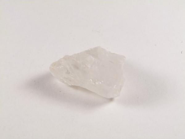 Przezroczysty, nieregularny kryształ kwarcu leżący na białym tle.