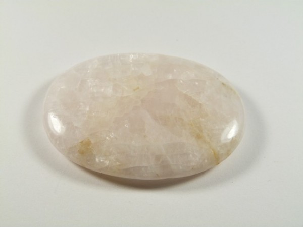 Kalcyt - kamień gładzony, polerowany, szlifowany. Gładki, owalny kamień kalcytu leży na białym tle.