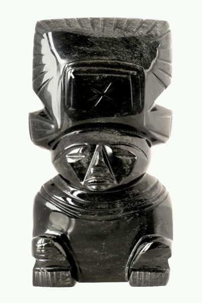 Czarna figurka z kamienia przedstawiająca stylizowaną postać siedzącą z dużą ozdobną czapką.