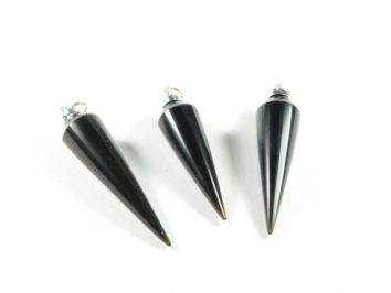 Trzy czarne wahadełka stożkowe z metalowymi oczkami leżące na białym tle.