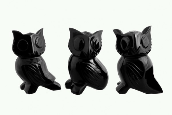 Trzy czarne figurki sów ustawione obok siebie na jasnym tle.