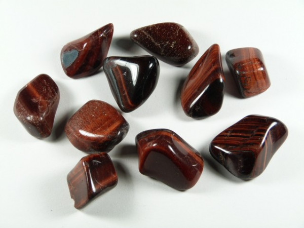 Dziesięć wypolerowanych kamieni o brunatno-czerwonym odcieniu leży na białym tle.