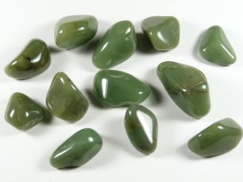 Zielone, oszlifowane kamienie nefrytu leżące na białym tle.