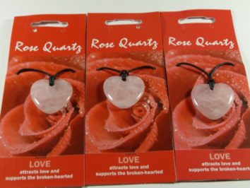Trzy naszyjniki z różowego kwarcu w kształcie serca na kartoniku z napisem "Rose Quartz".