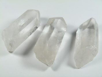 Trzy przezroczyste kryształy kwarcu leżące na białym tle.