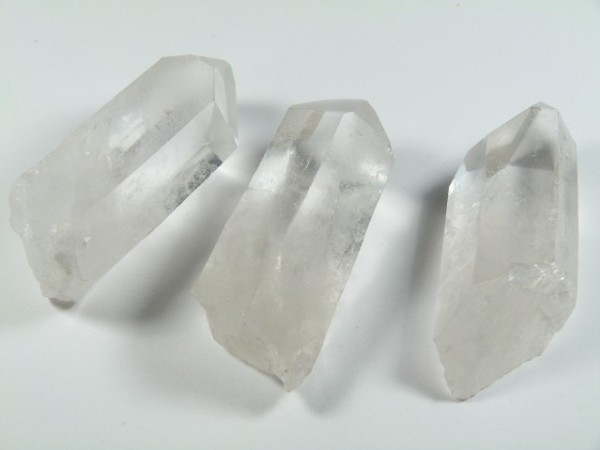 Trzy przezroczyste kryształy kwarcu leżące na białym tle.