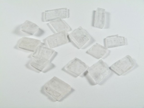 Spar islandzki - kamień naturalny, surowy, nieszlifowany. Kilka białych kryształków na białym tle.