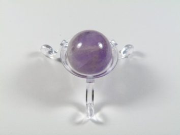 Kula ametyst szlifowany średnica 2,5 cm. Fioletowa kulka ametystu na przezroczystej podstawce, na białym tle.